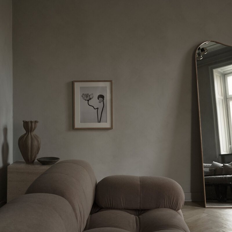 A beige living room featuring a beige camaleonda bb italia sofa and a mirror partially visible. Additionally, there's an art print in an oak frame depicting two poppy flowers in black and white
